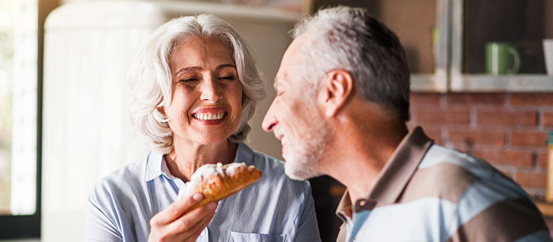 Older Woman Feeding Baked Good to Older Man and shows off gum contouring